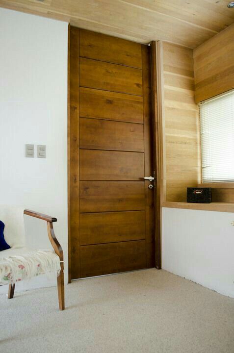 a chair sitting in front of a wooden door on top of a white wall next to a window