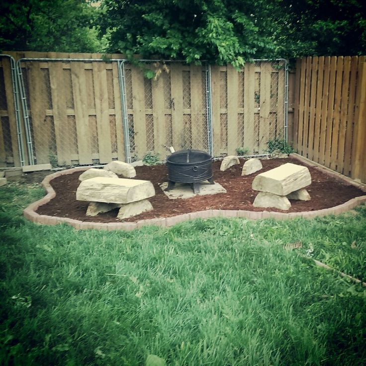 a backyard with a fire pit in the middle and some rocks on the other side