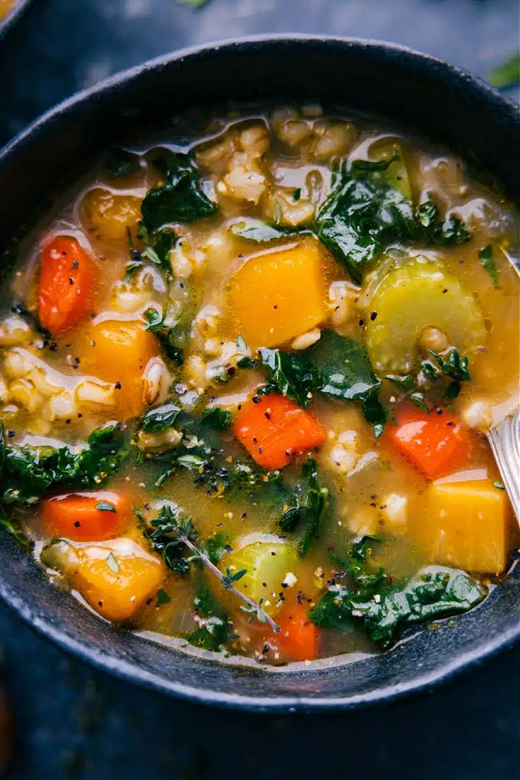 a bowl of soup with carrots, kale and other vegetables