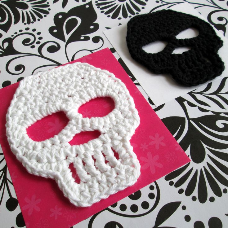 a crocheted skull on a pink card next to a black and white mask