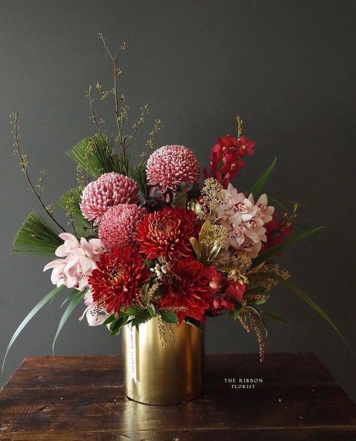 a gold vase filled with flowers on top of a wooden table