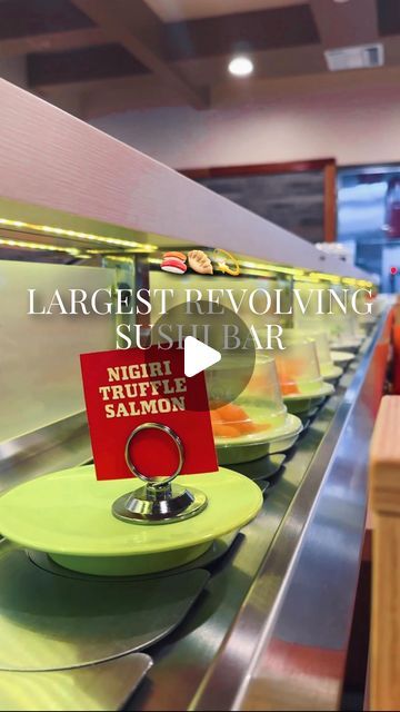 a restaurant counter with plates and signs on the trays that say, largest revolving sushi bar