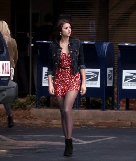 a woman in a red dress and black jacket crossing the street with her legs crossed