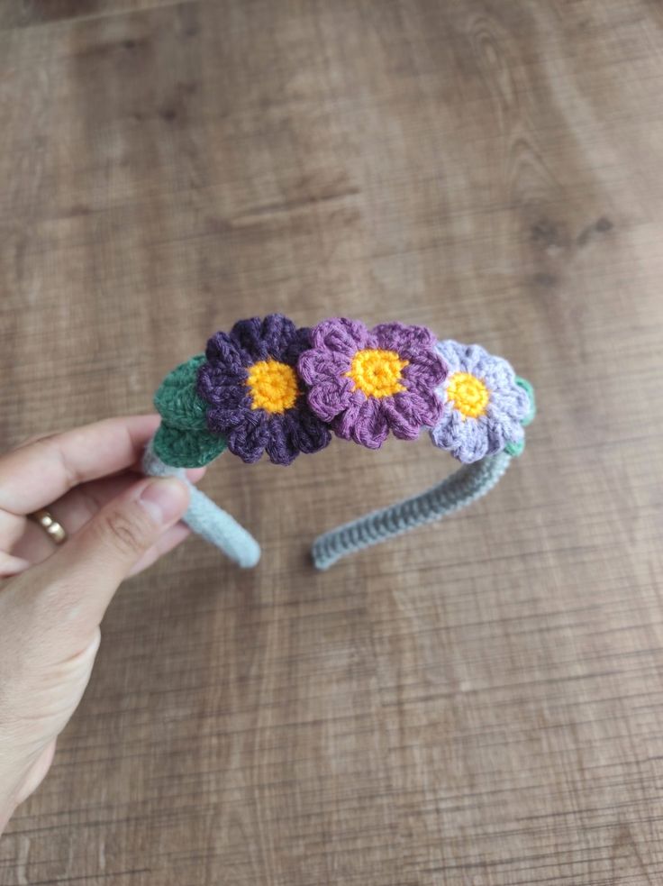 a crocheted flower headband is being held by a woman's hand