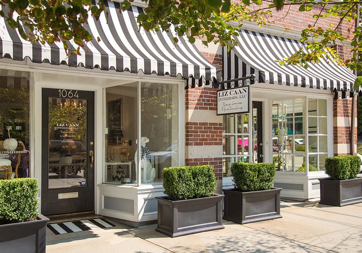 a store front with black and white awnings on the windows, potted plants outside