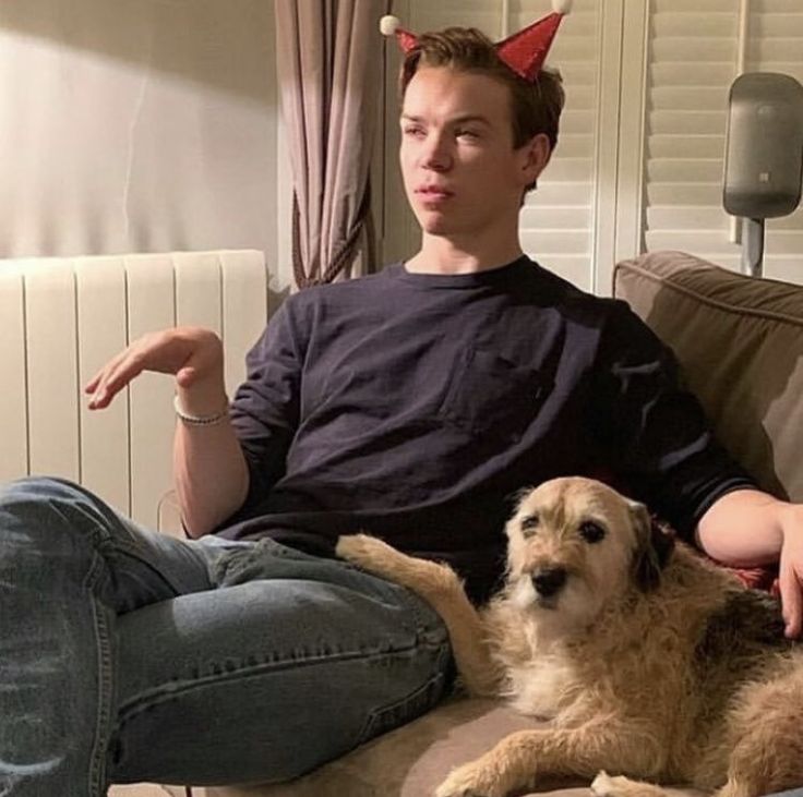 a man sitting on top of a couch next to a brown dog wearing devil horns