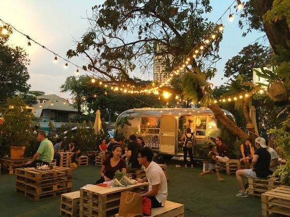 people sitting at picnic tables in front of an airstream with lights strung over it