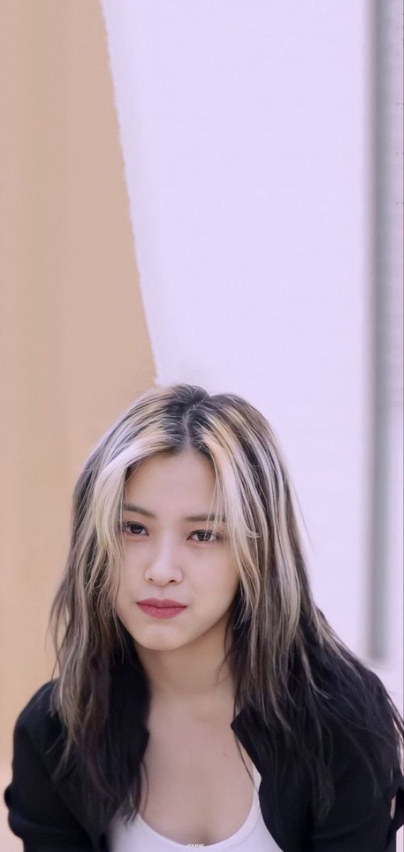 a young woman with long hair standing in front of a white and tan wall wearing a black jacket