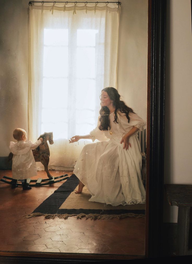 a woman sitting in front of a mirror next to a child on a rocking horse