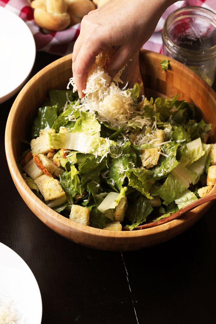 a person scooping cheese into a salad in a wooden bowl with the words good cheap eats caesar salad