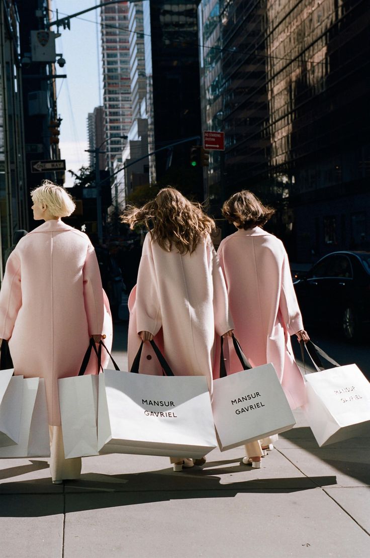 three women in pink coats carrying shopping bags