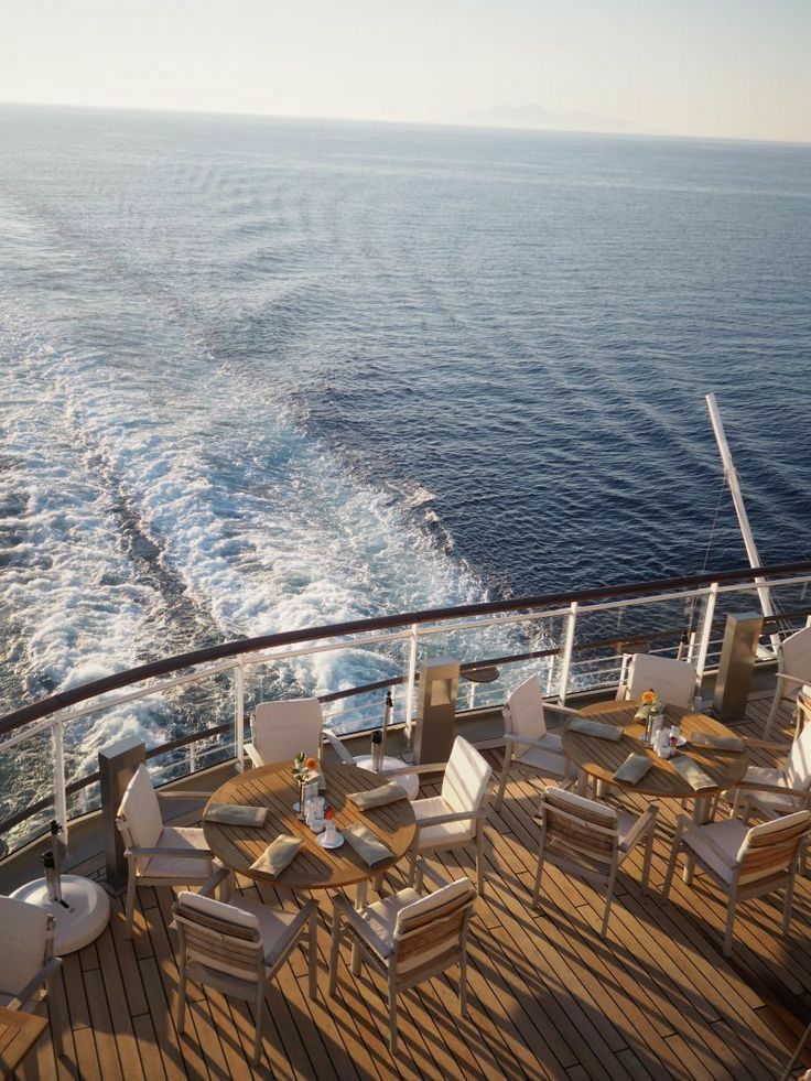 the deck of a cruise ship with tables and chairs on it, overlooking the ocean