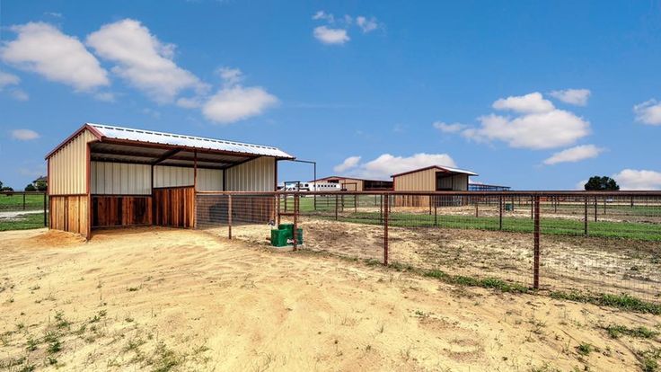 a horse barn with two stalls and a fence in the foreground, on a dirt field