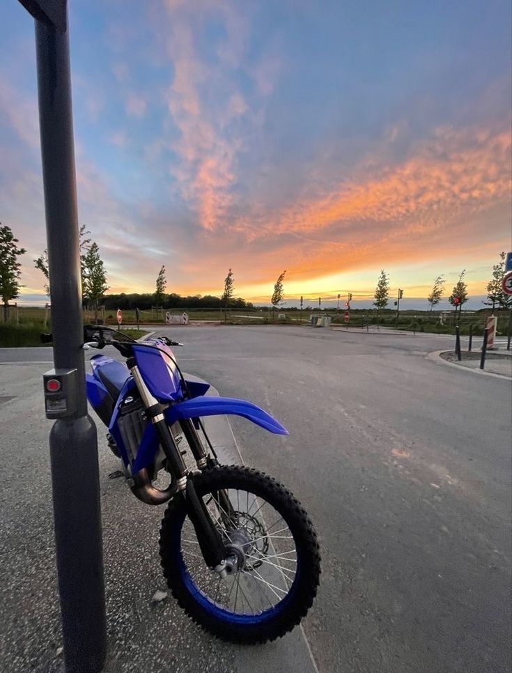 a blue dirt bike parked next to a pole on the side of the road at sunset