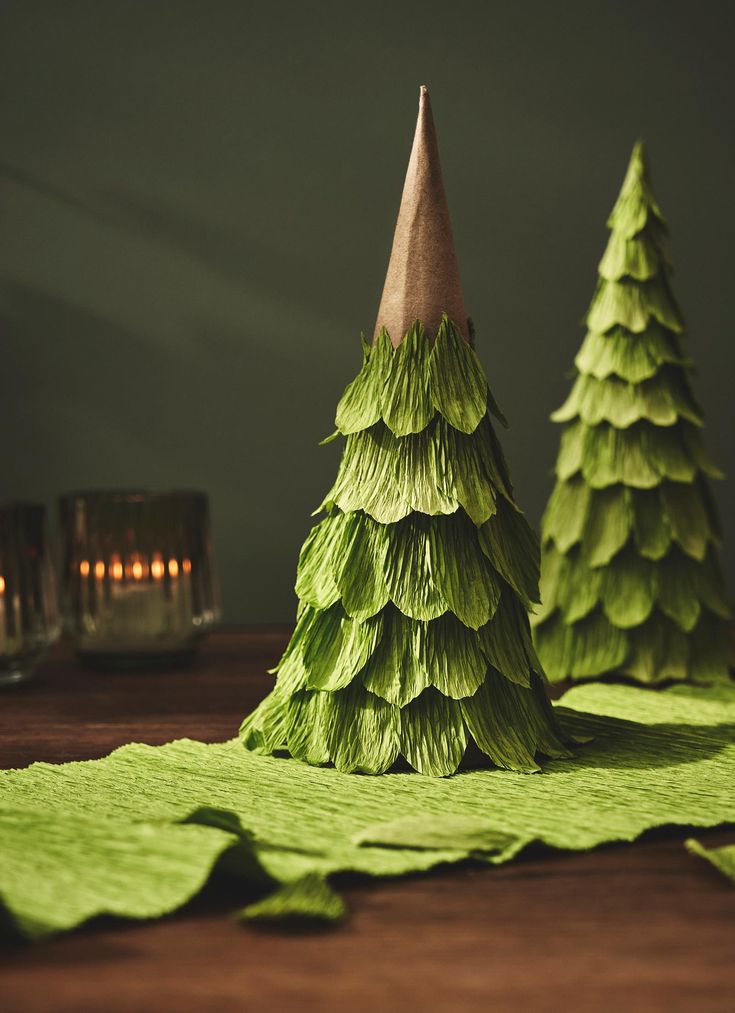 two paper christmas trees sitting on top of a wooden table