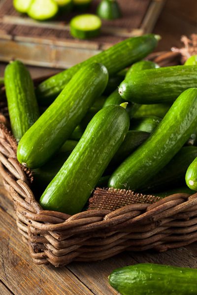 a basket filled with green cucumbers sitting on top of a wooden table