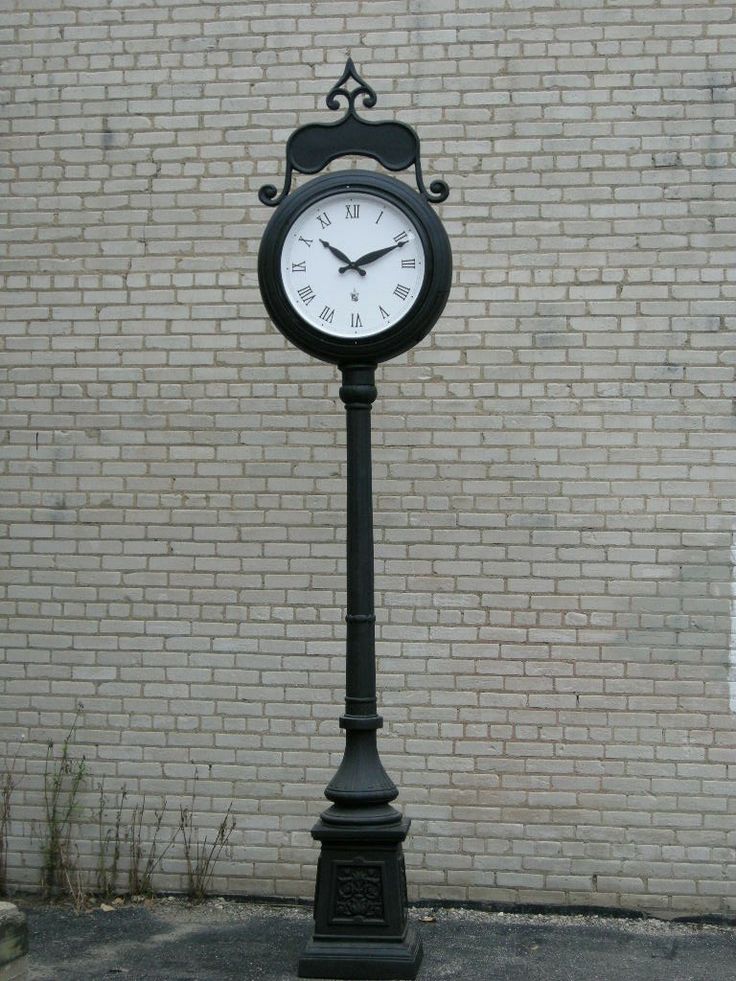 a clock on a pole in front of a brick wall