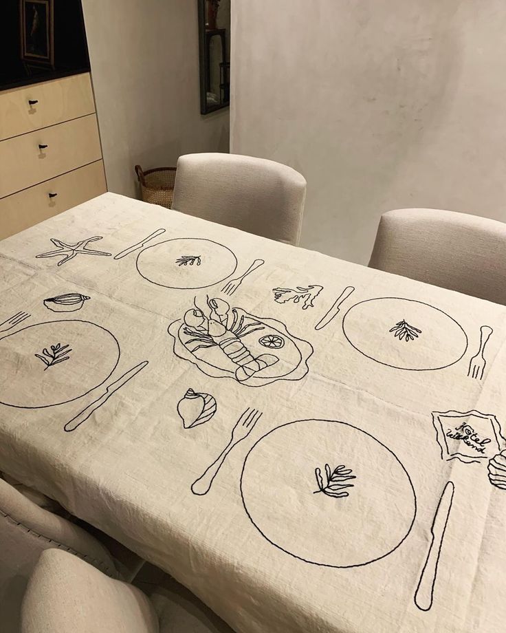 the table cloth has drawings on it and is set with four white chairs around it