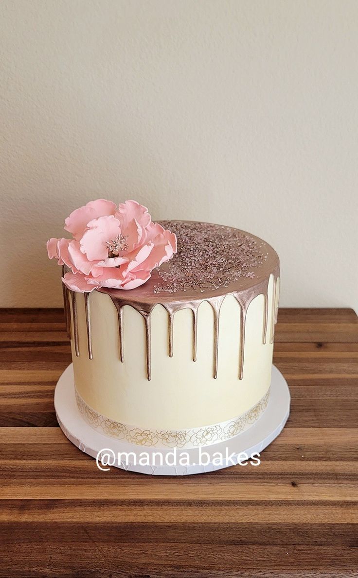 there is a cake with icing and a flower on the top, sitting on a wooden table