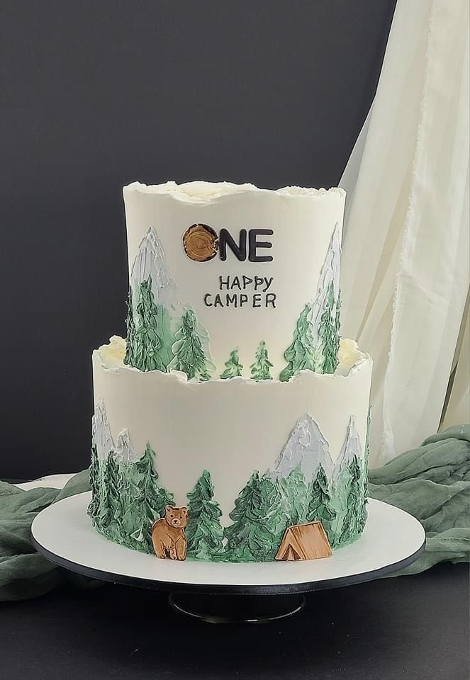 two tiered cake decorated with trees and bears on it's side that says one happy camper