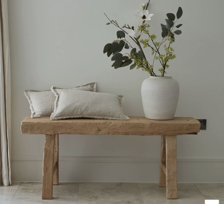 a wooden bench with two pillows and a vase filled with flowers sitting on top of it