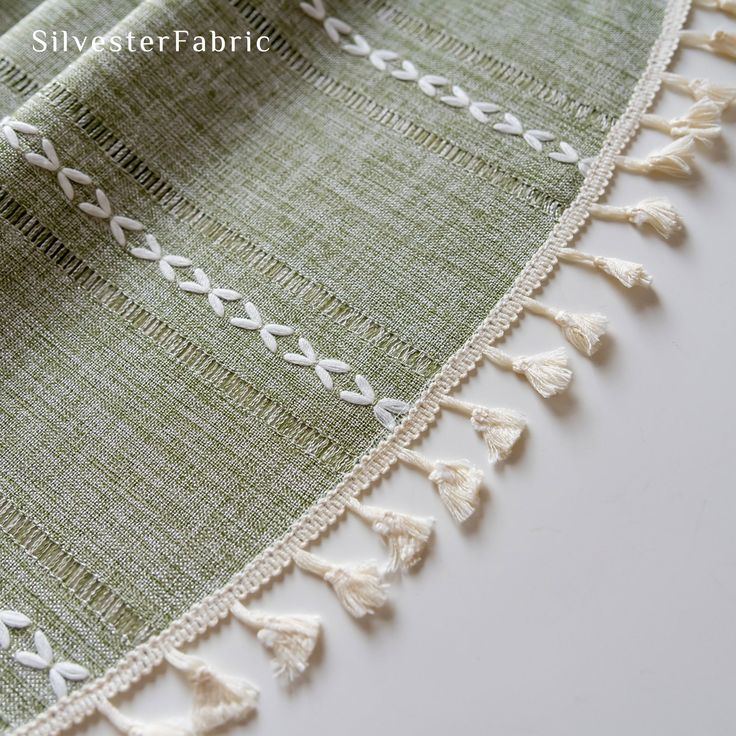 closeup of the edge of a green and white table cloth with tassels