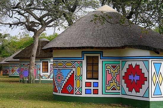 colorfully painted huts line the grass in front of trees