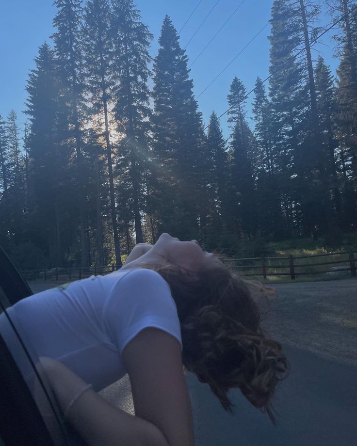 a woman laying her head on the window of a car in front of some trees