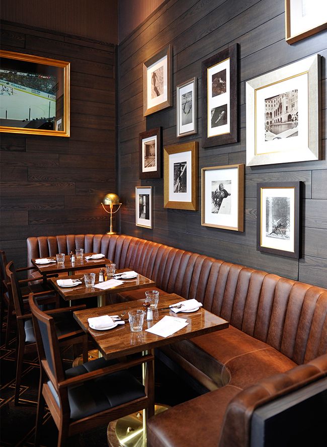 a restaurant booth with leather booths and framed pictures on the wall, along with wine glasses