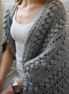 a woman is wearing a gray crocheted cardigan