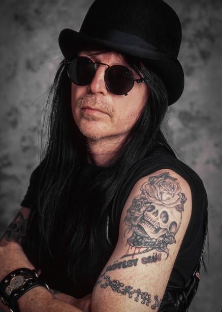 a man with long black hair wearing sunglasses and a hat on his head is posing for the camera