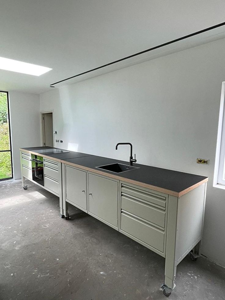 an empty kitchen with a sink and counter top in the middle of it, next to a large window