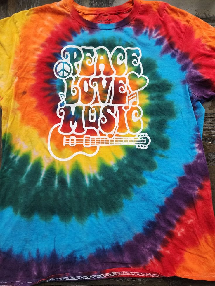 This tie dye is our Peace, Love, Music standard. These shirts are done on Gildan brand tees and are super comfortable. Available in sizes S-2X. Please note, while most orders of our standard dyes ship next day - if your size is out of stock it will be 5-7 days for shipping. Due to the nature of tie dye and screen printing, there will be slight variations in each shirt. Multicolor Hippie T-shirt With Letter Print, Hippie Multicolor Letter Print T-shirt, Summer Band Merch Tie Dye T-shirt, Casual Multicolor T-shirt For Music Festival, Hippie Multicolor Screen Print T-shirt, Multicolor Hippie T-shirt With Screen Print, Hippie Cotton T-shirt For Music Festival, Multicolor Crew Neck T-shirt For Music Festival, Cotton Tie Dye Tops For Music Festival