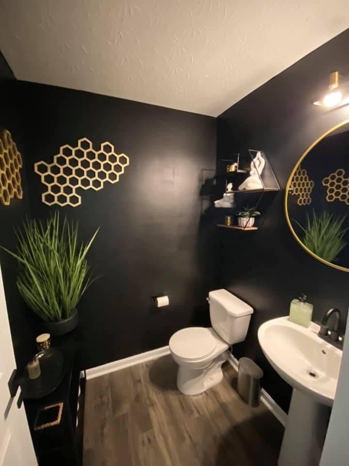 a bathroom with black walls and gold accents on the wall above the toilet is decorated with potted plants