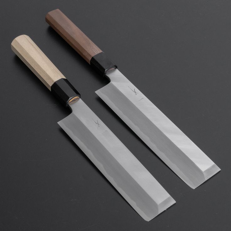 two knives are next to each other on a black surface, one has a wooden handle