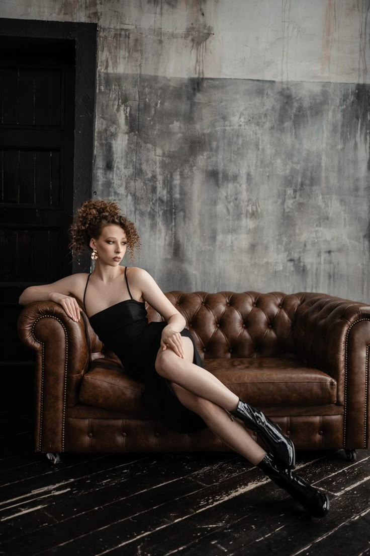 a woman sitting on top of a brown couch in front of a wall and floor