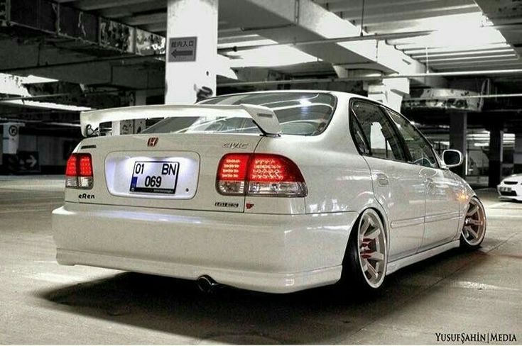 the rear end of a white car parked in a parking garage with other cars behind it