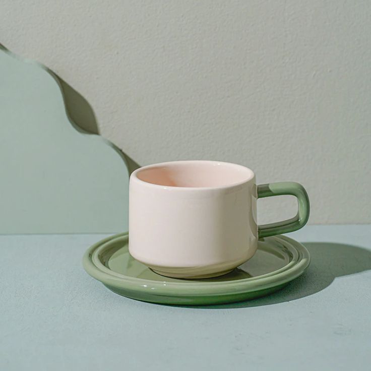 a white cup and saucer sitting on a green plate next to a gray wall