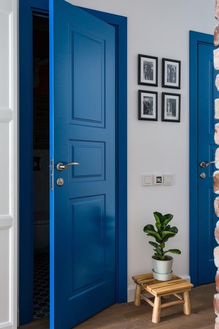 a blue door in a white room with pictures on the wall and potted plant