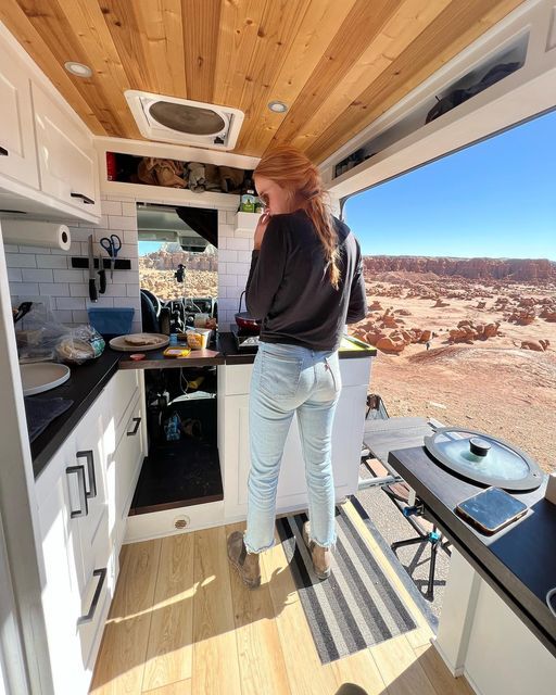 a woman standing in the kitchen area of a camper with an open stove top