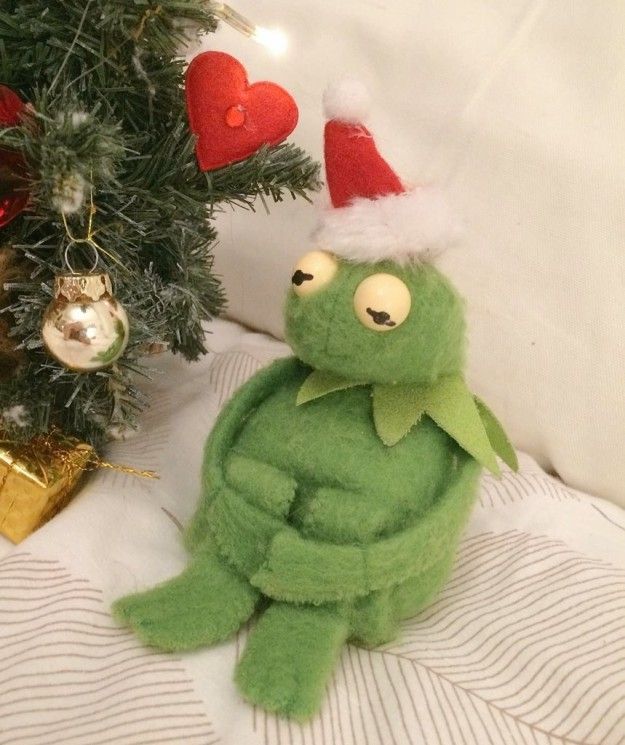 a green stuffed animal sitting next to a christmas tree