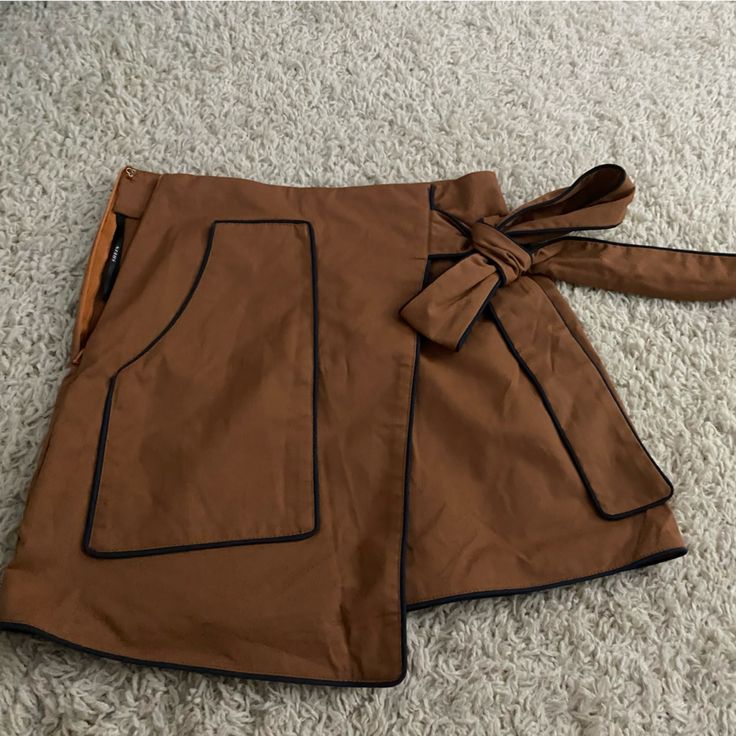 Super Cute Asymmetrical Decorative Side Tie Skirt. Never Worn. Caramel Brown With A Navy/Black Trim With Zipper On The Side Brown Asymmetrical Skirt For Workwear, Brown Asymmetrical Skirt For Work, Chic Asymmetrical Skort With Pockets, Brown Asymmetrical Skirt For Fall, Casual Brown Asymmetrical Skirt, High Waist Brown Skort With Pockets, Brown Lined Mini Skort, Trendy Brown Skort With Pockets, High Waist Brown Skirt For Night Out