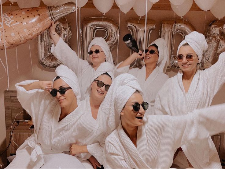 a group of women in white robes are posing for a photo with balloons behind them