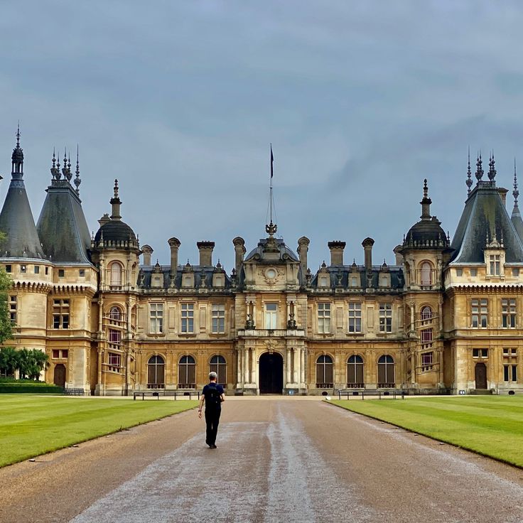 a man walking down a dirt road in front of a large building