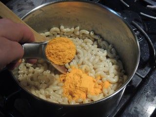 a person stirring macaroni and cheese in a pot on the stove with a wooden spoon