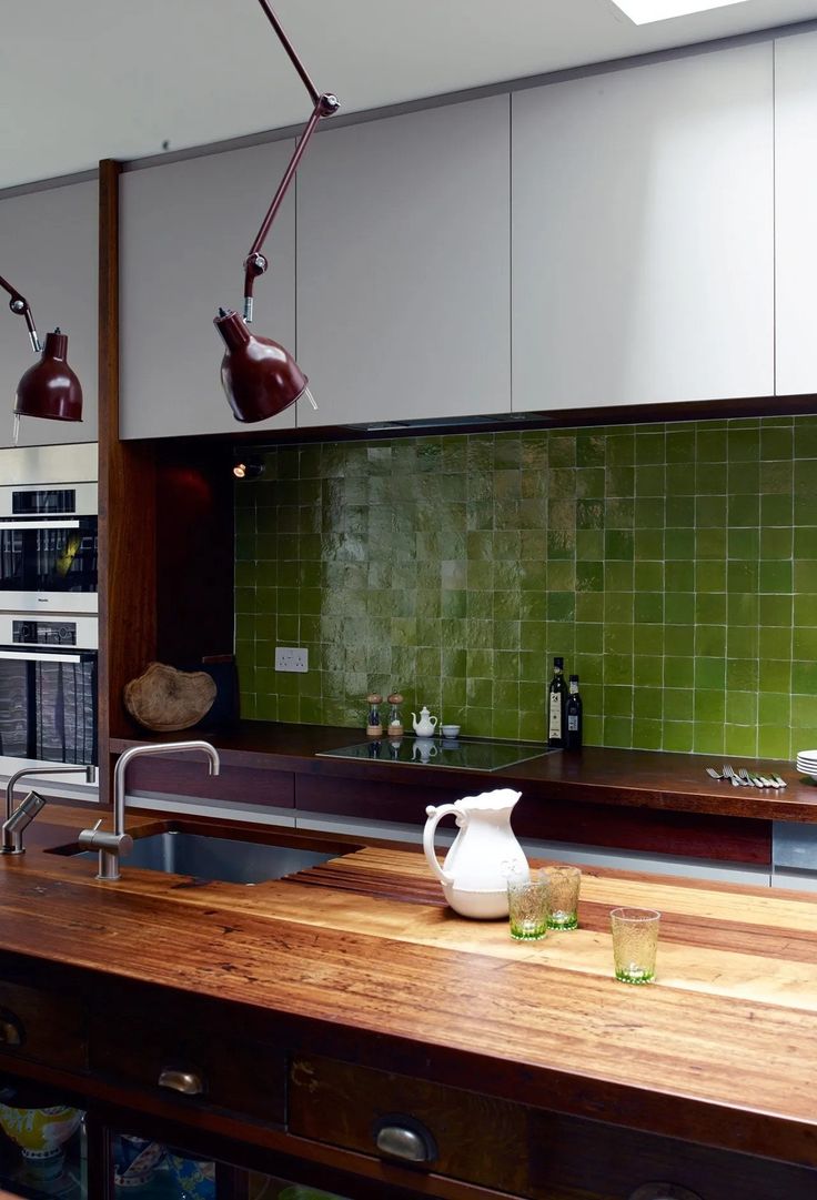 a kitchen with green tile backsplash and wooden counter tops, two hanging lights above the sink