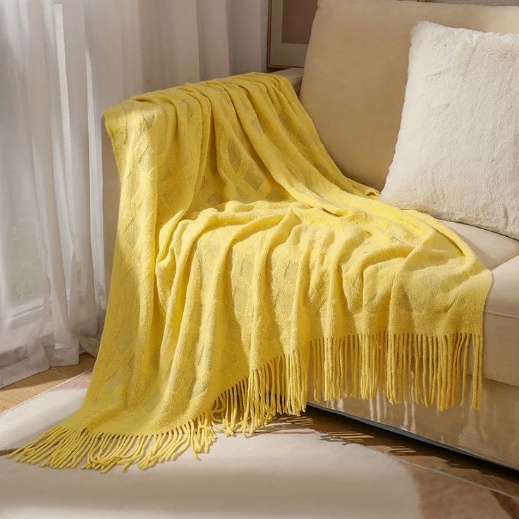 a couch with a yellow blanket on top of it next to a white rug and window