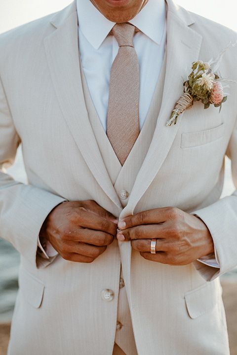 a man in a white suit and tie with his hands on his lapel pocket