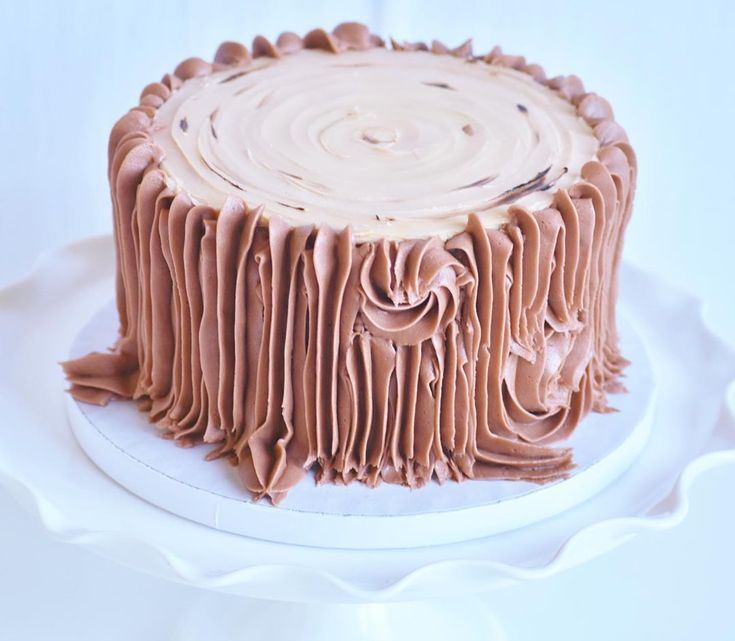 a chocolate cake with frosting on a white platter, ready to be eaten