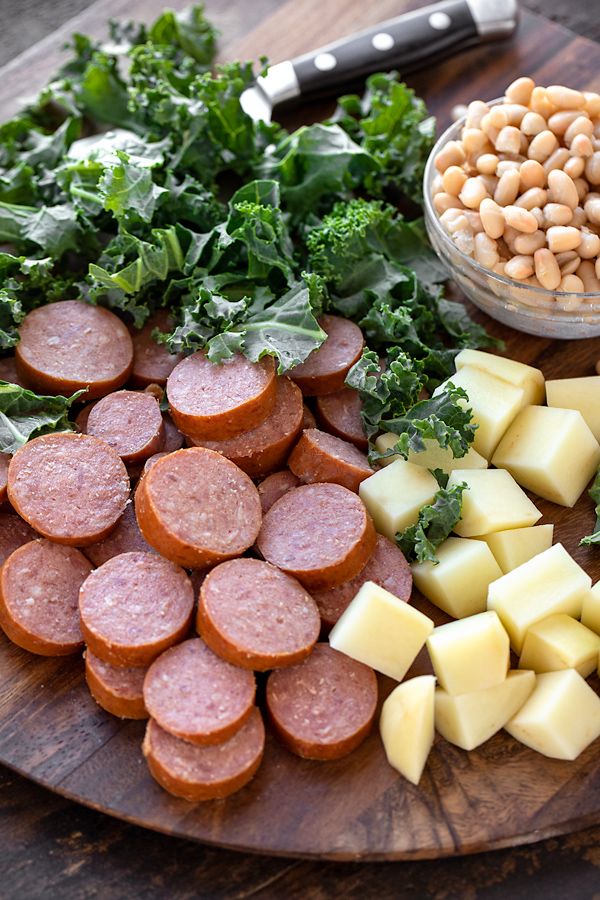 a wooden plate topped with sausages, potatoes and greens